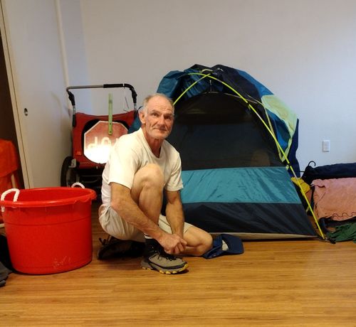 Mikey sitting on the floor of his new apartment with a bike trailer and tent.